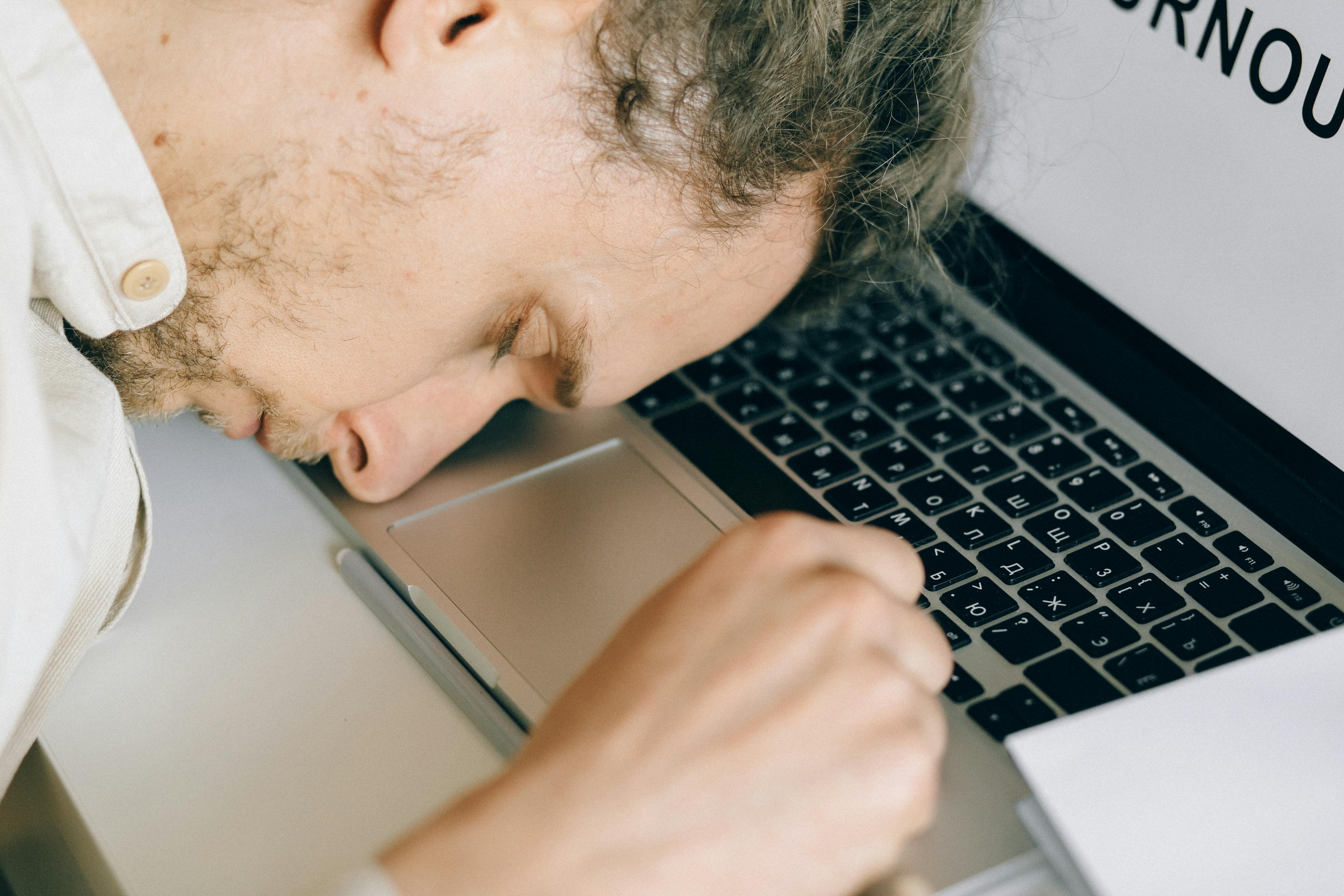Erschöpfter Mensch am Schreibtisch mit Laptop — Burnout im Berufsalltag